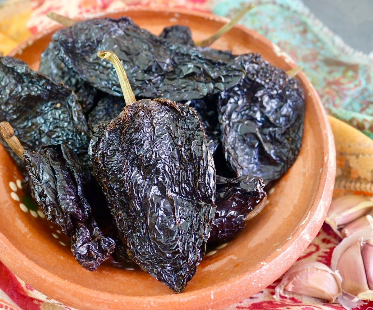 Several Ancho chiles in a terra cotta bowl.