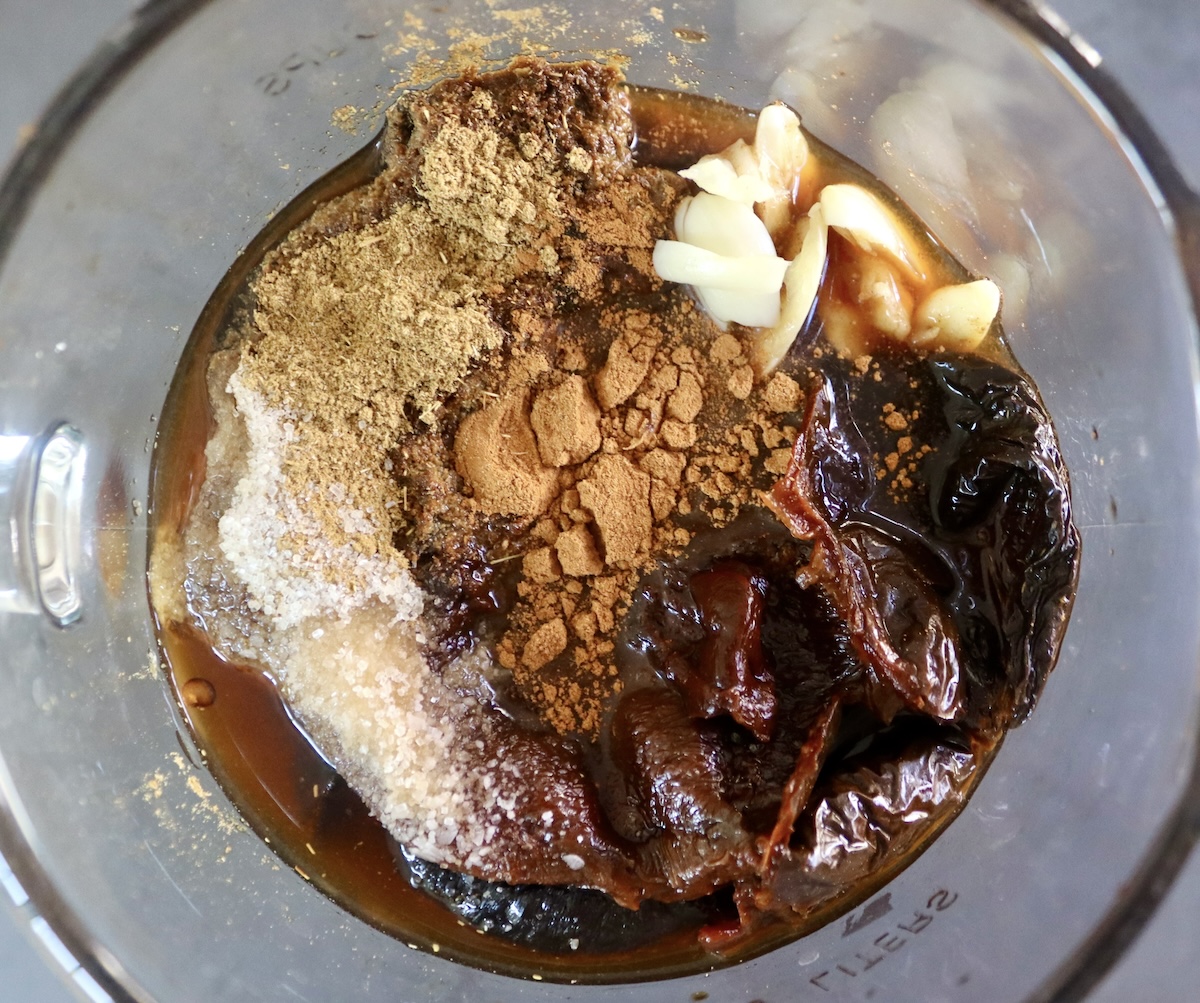 Ingredients for ancho chile sauce in a blender including cinnamon, cumin, garlic, ancho chiles and vegetable stock.