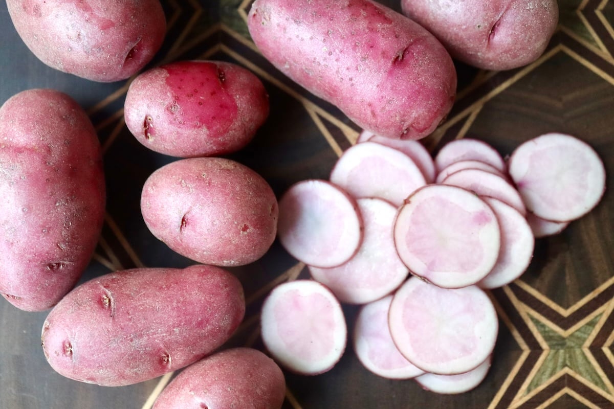 Whole and sliced ping fingerling potatoes on a dark wood-patterned cutting board.