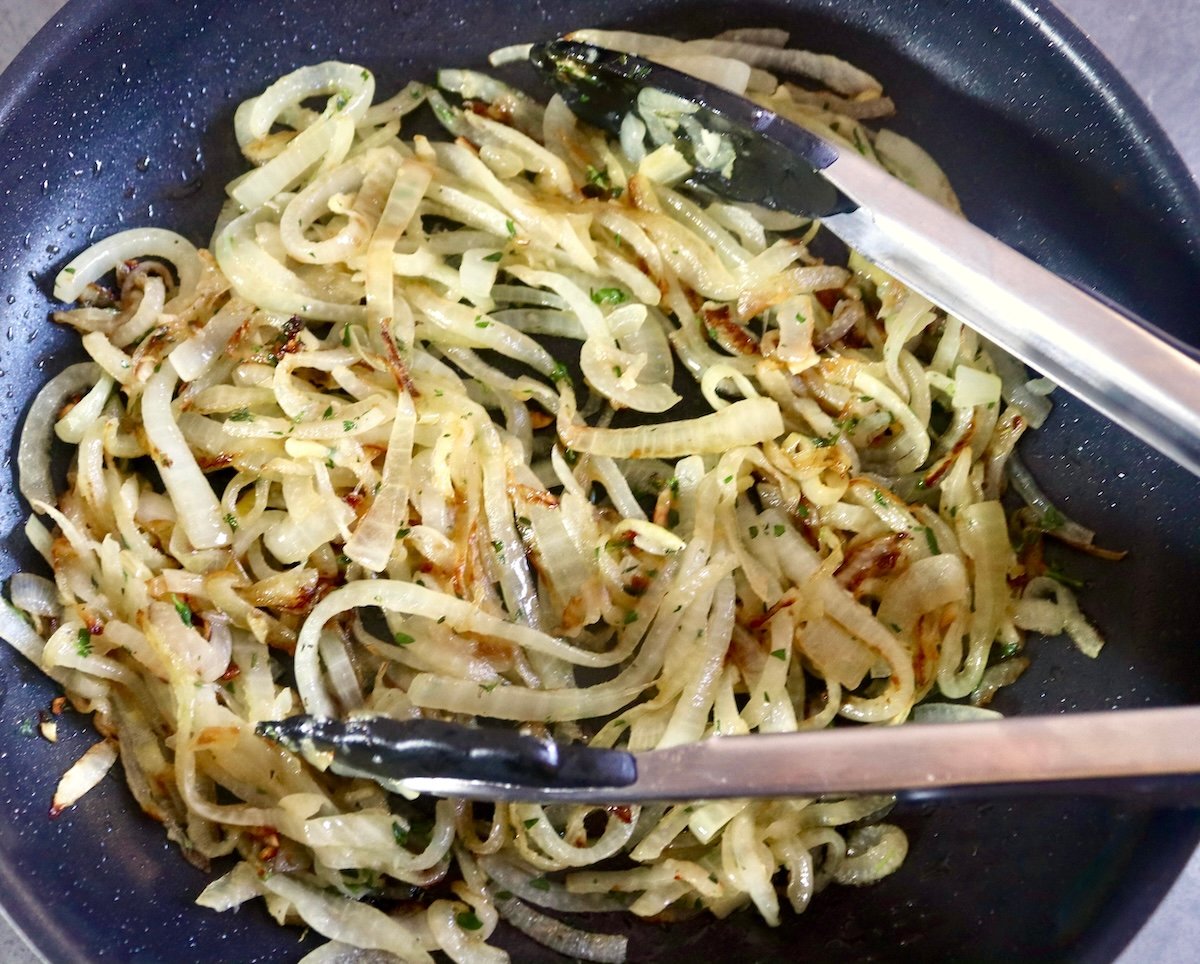 Caramelized onions in a skillet with tongs.