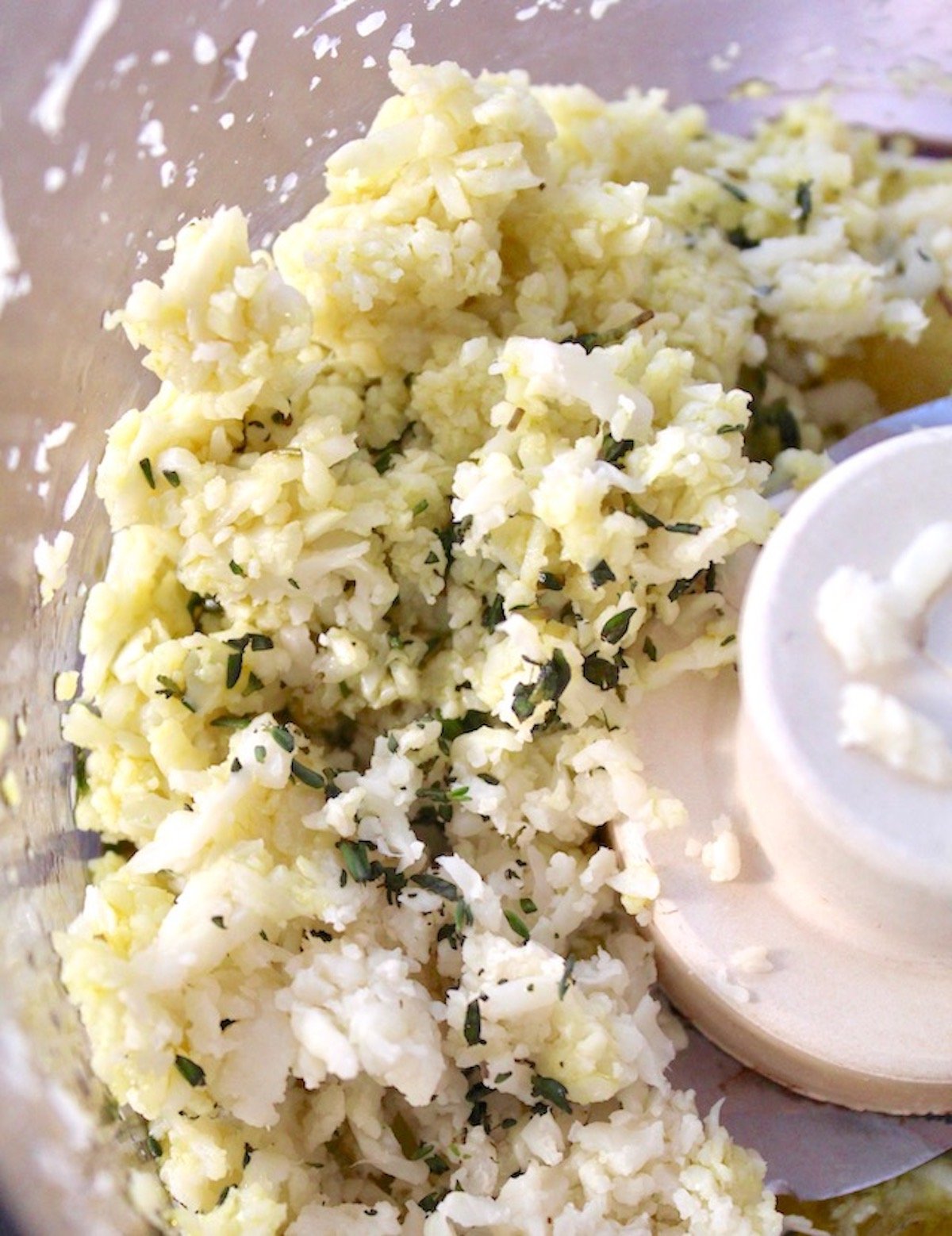 Riced cauliflower in food processor with herbs.