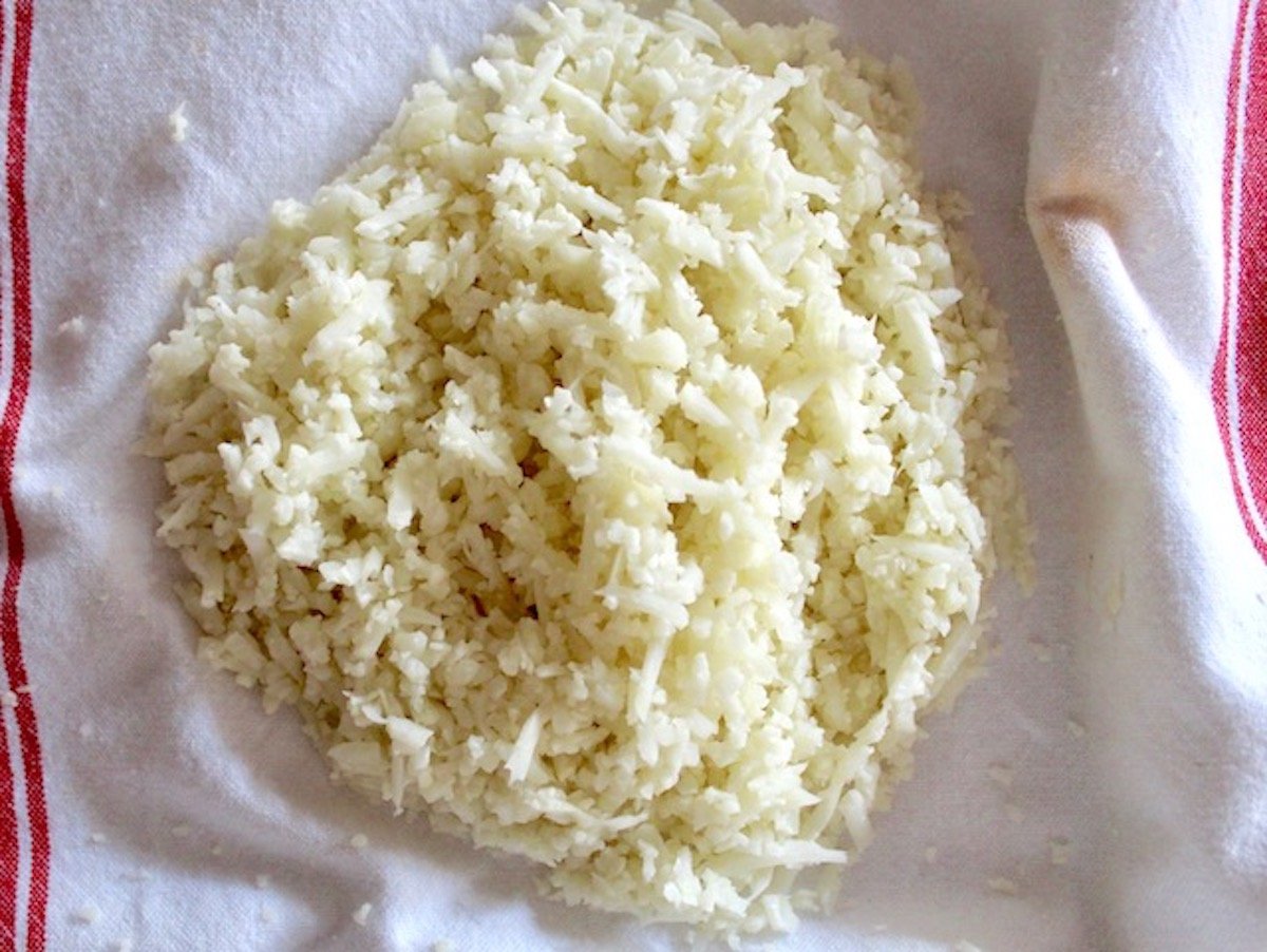 Pile of riced cauliflower on a white and red kitchen towel.