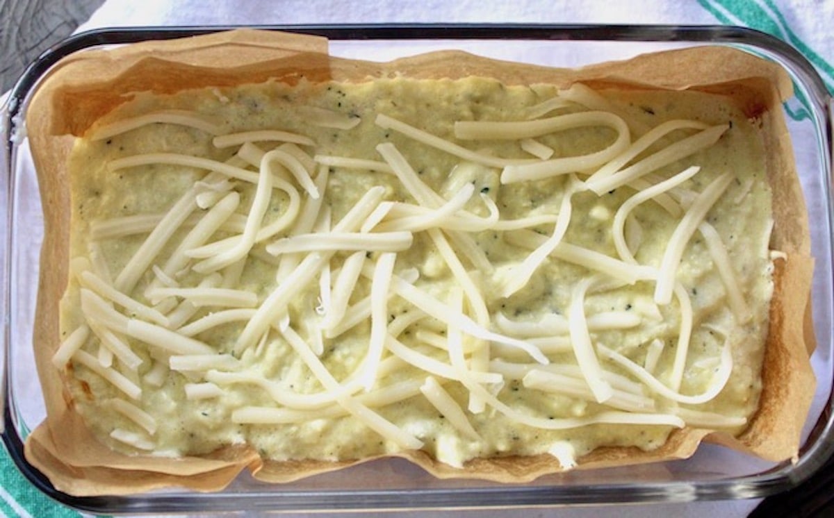 Batter for cauliflower bread in a loaf pan with grated white cheese on top.