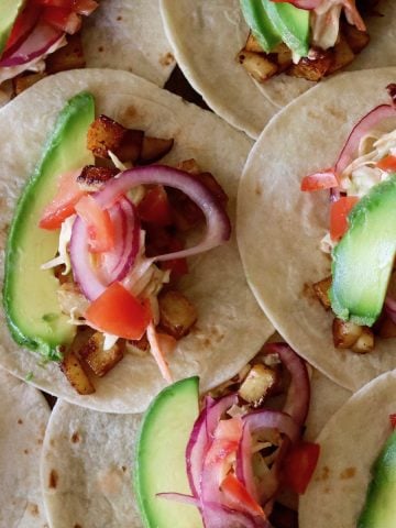 Several tortillas with cubed spicy potato, avocado, lime slices and pickled onions.