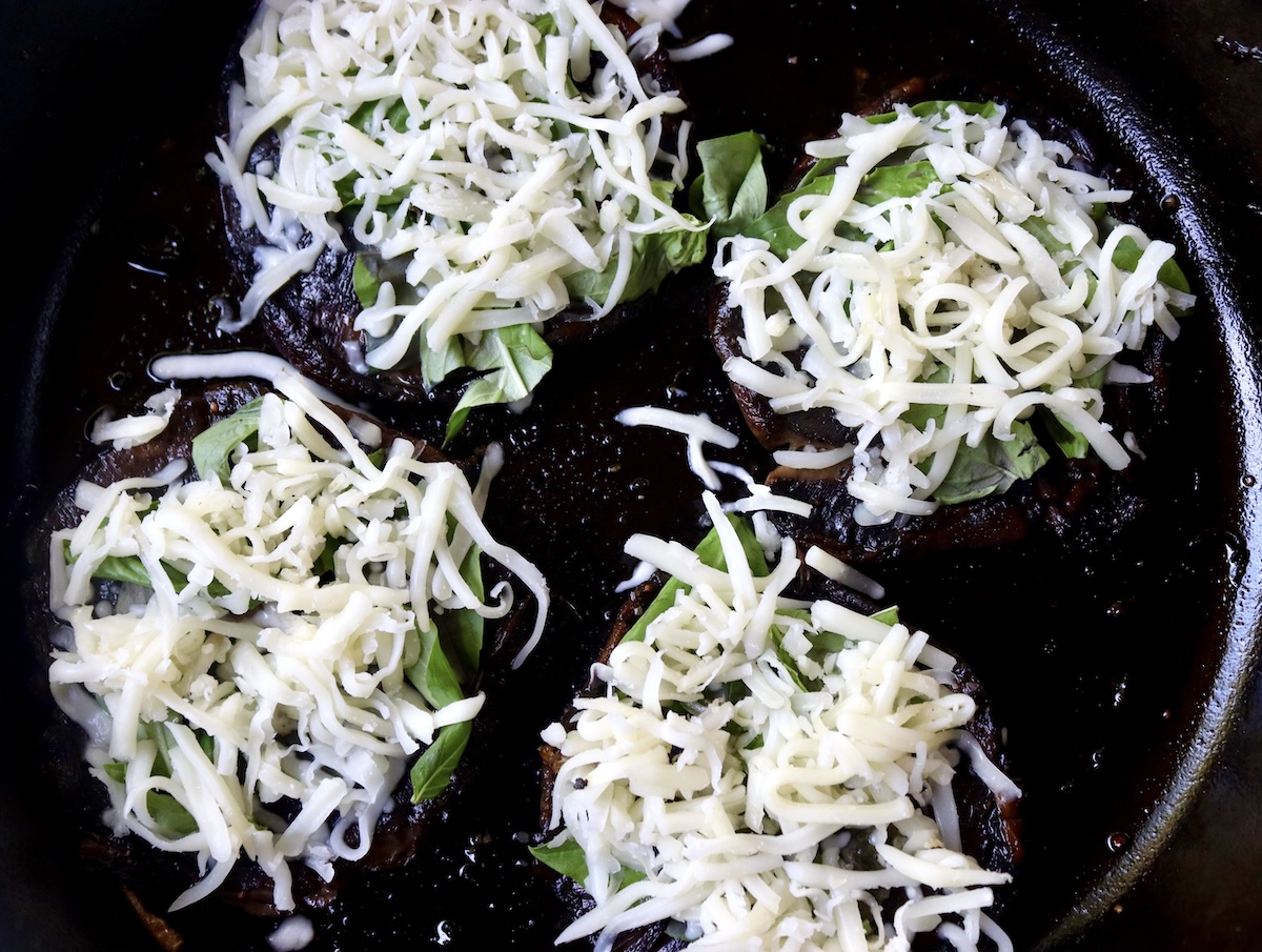 Portobello mushroom caps with basil leaves and grated mozzarella.