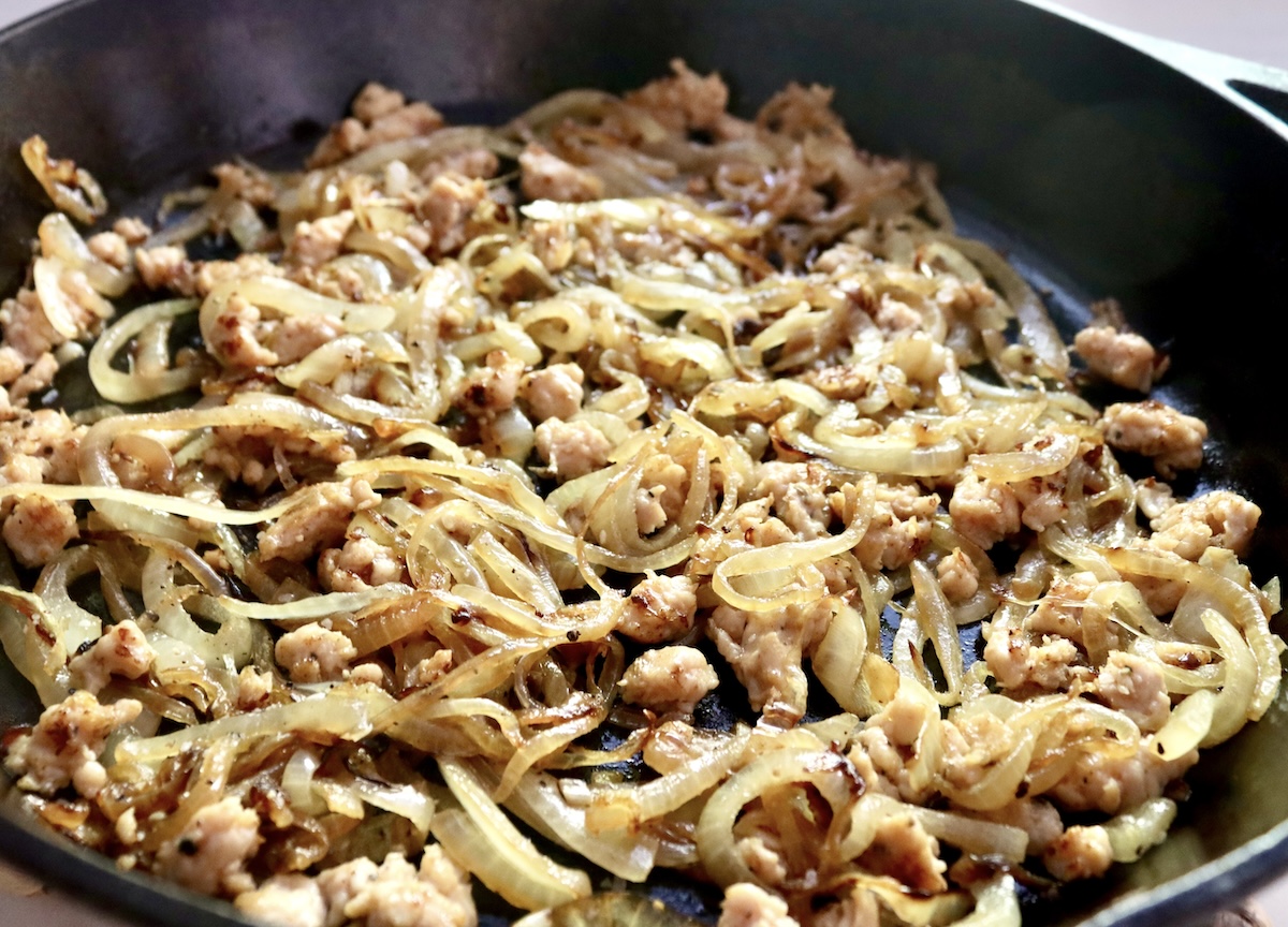 Mixture of onion and sausage in a cast iron skillet.
