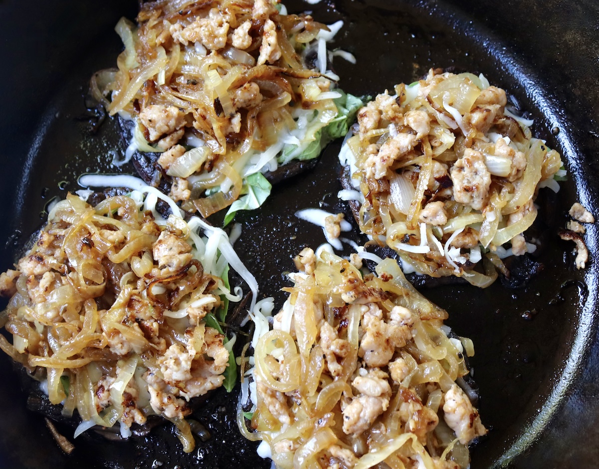 Portobello mushroom caps with basil leaves, grated mozzarella, onions and sausage.