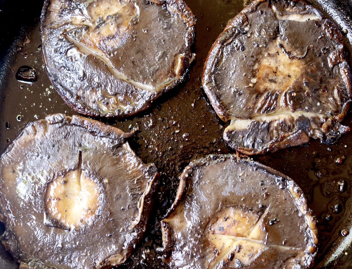 4 cooked portobello mushrooms in a cast iron skillet, round side down.