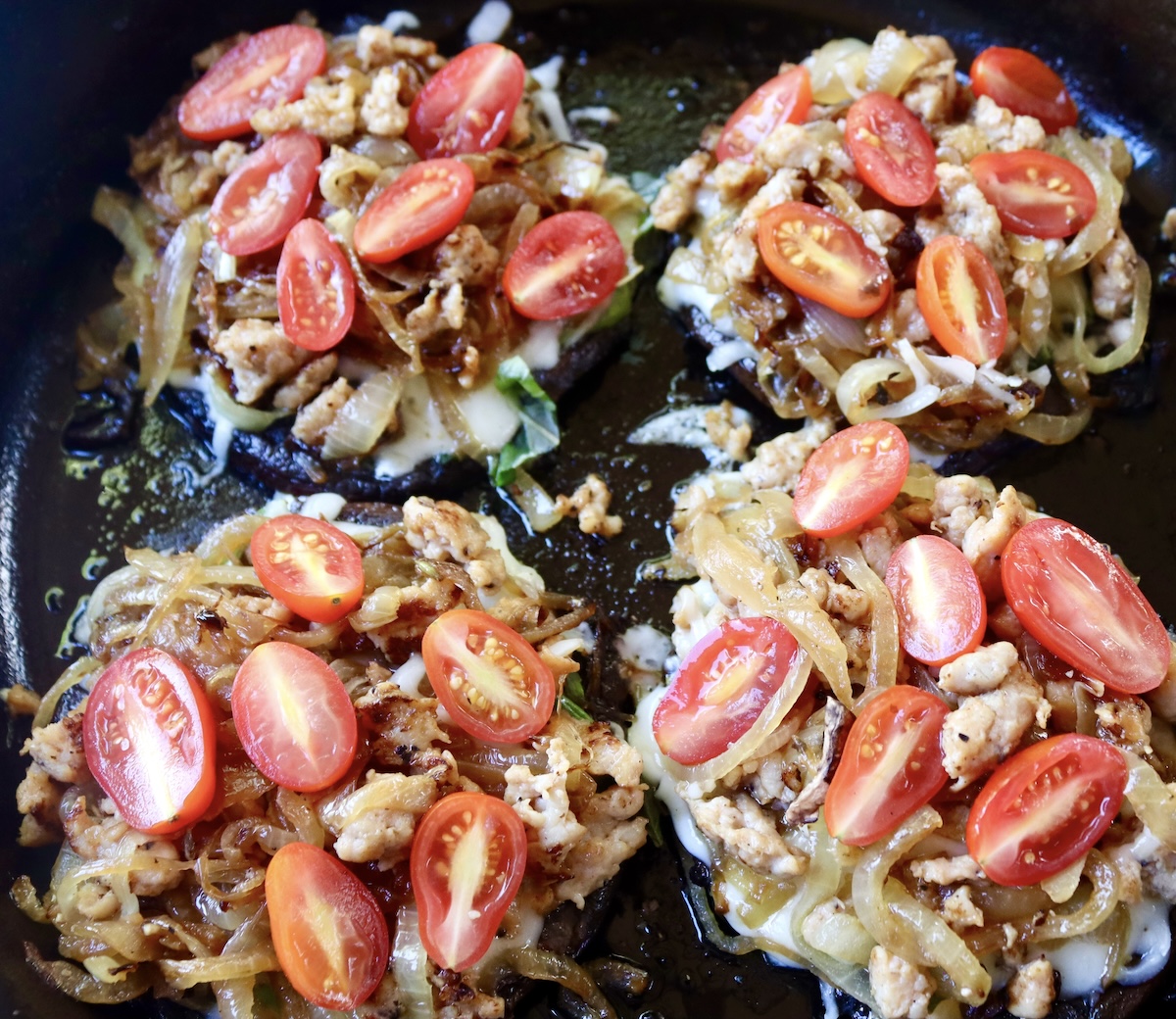 Portobello mushroom caps with basil leaves, grated mozzarella, onions, sausage and sliced teardrop tomatoes.
