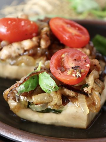 Three portions of Portobello Mushroom Pizza on a black ceramic plate, with caramelized onion, sausage, basil and tomatoes.
