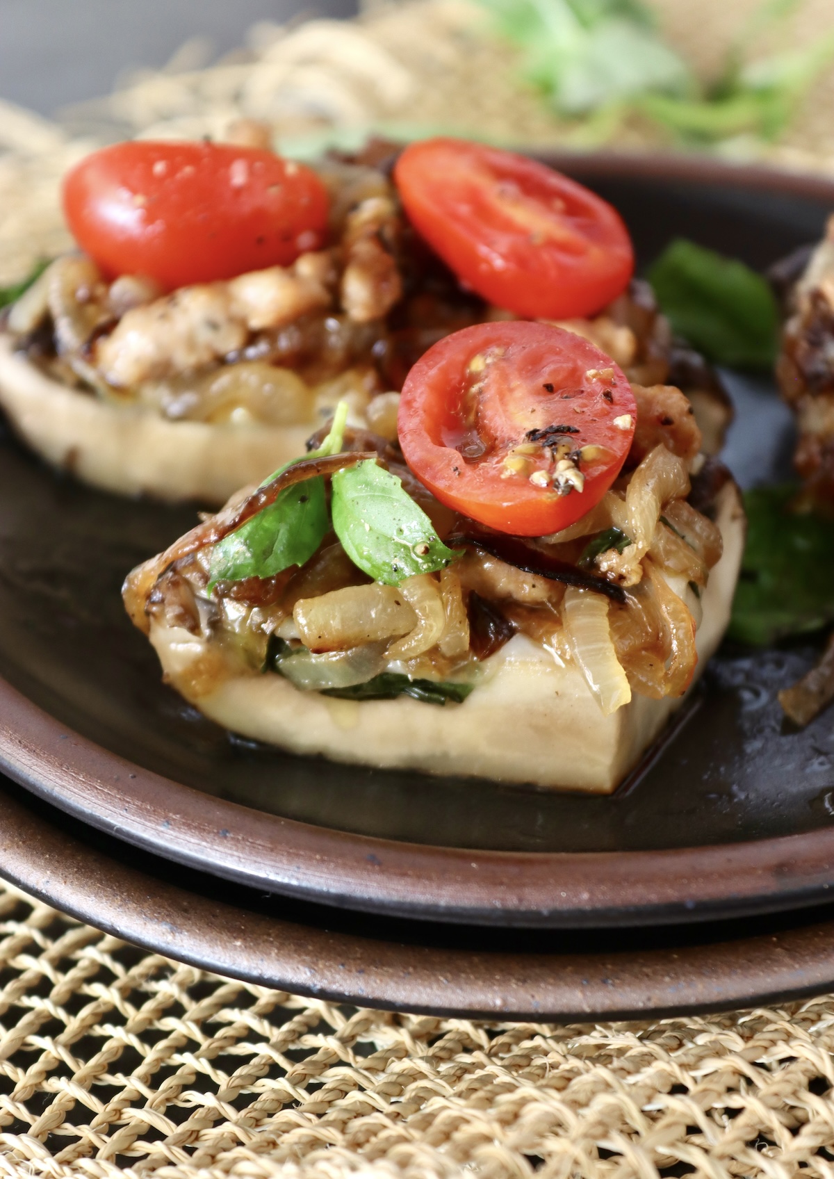 Three portions of Portobello Mushroom Pizza on a black ceramic plate, with caramelized onion, sausage, basil and tomatoes.