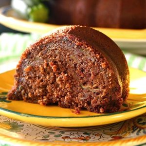 Large slice of chocolate zucchini bundt cake on a golden-colored, ceramic plate.