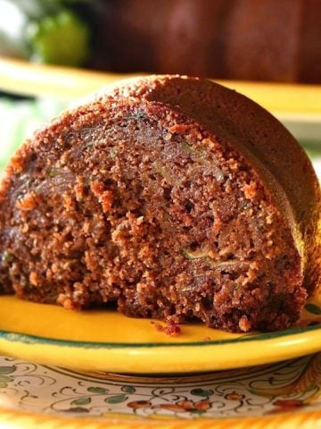 Large slice of chocolate zucchini bundt cake on a golden-colored, ceramic plate.