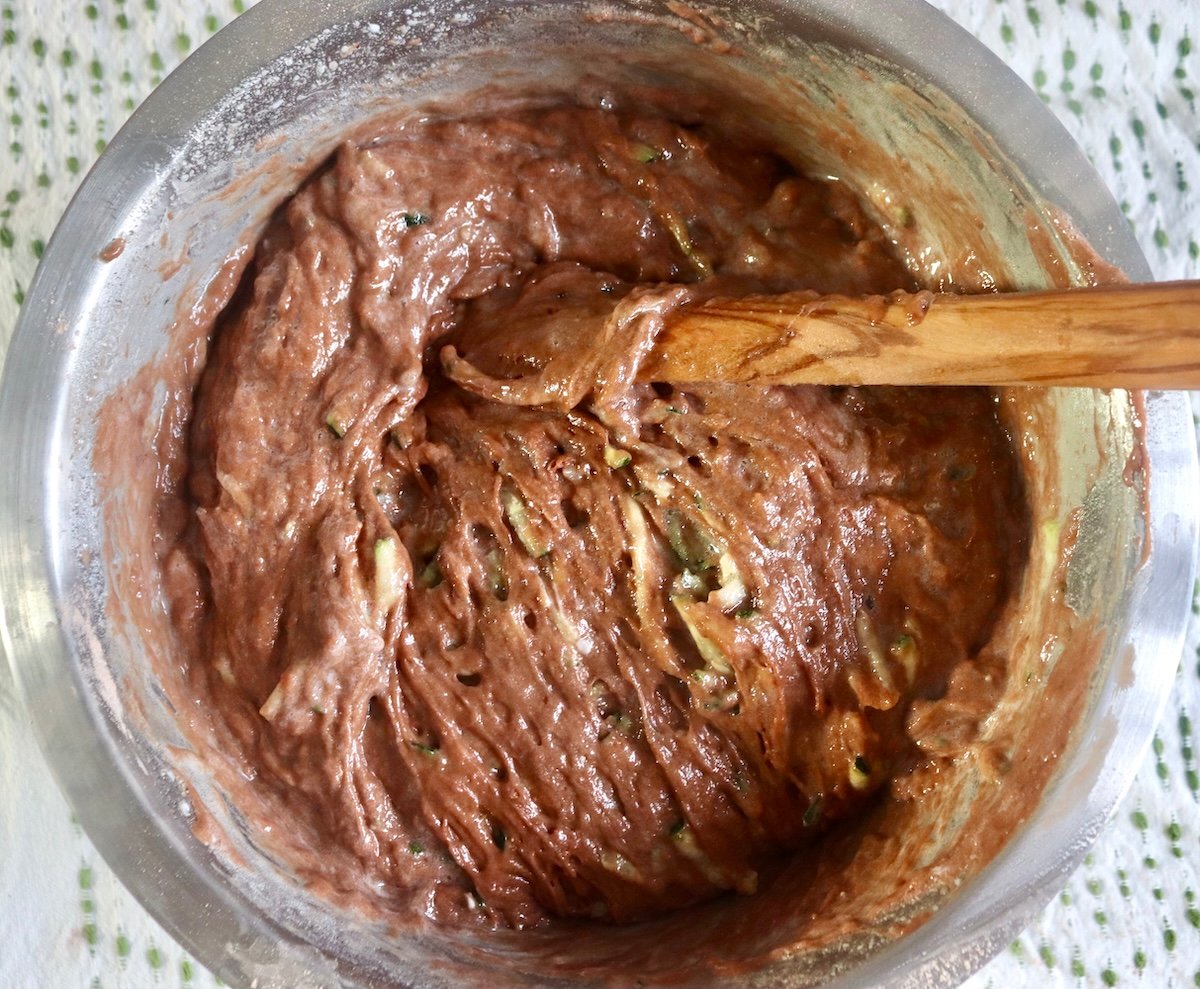 Mixed chocolate zucchini batter with a wooden spoon in a stainless steel bowl.