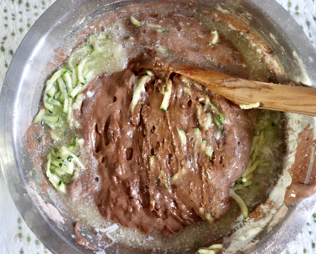 Chocolate zucchini batter being mixed with a wooden spoon.