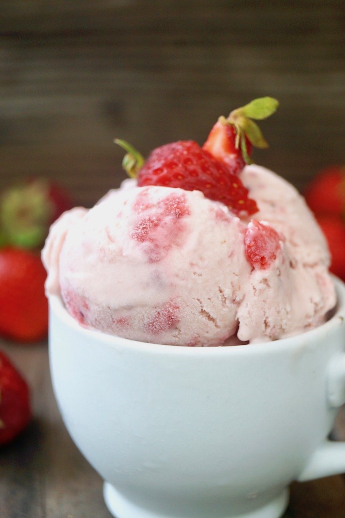 Close up, side view of Strawberry Swirl No-Churn Ice Cream in a small white mug with strawberry on top.