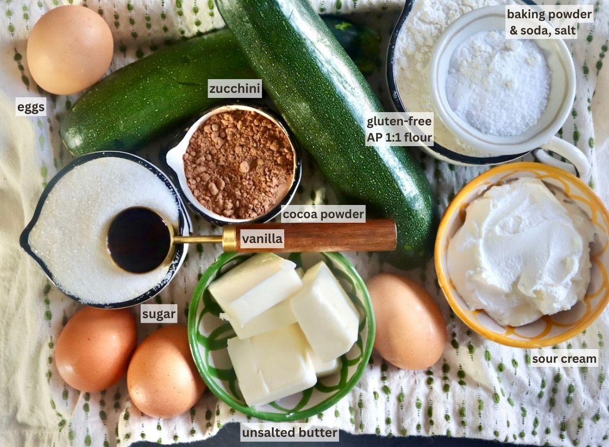 Ingredients for chocolate zucchini cake including zucchini, butter, cocoa powder, sugar, salt, sour cream, vanilla, eggs and flour.