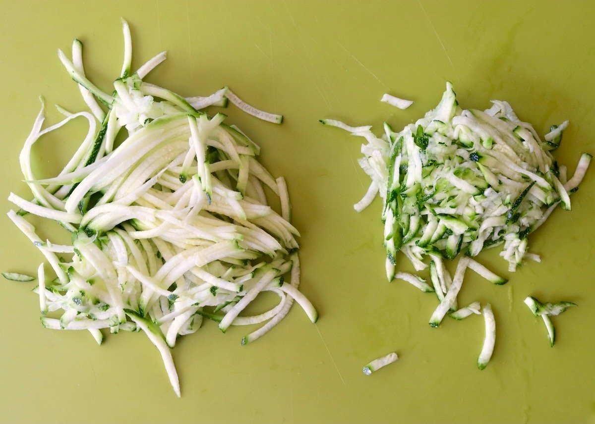 Two piles of grated zucchini -- one has been drained of liquied and is smaller, on a green cutting board.