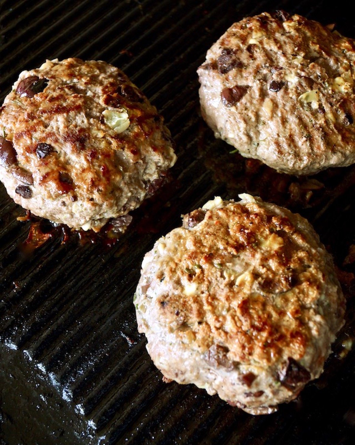 Three Grilled Greek Burgers on the grill.