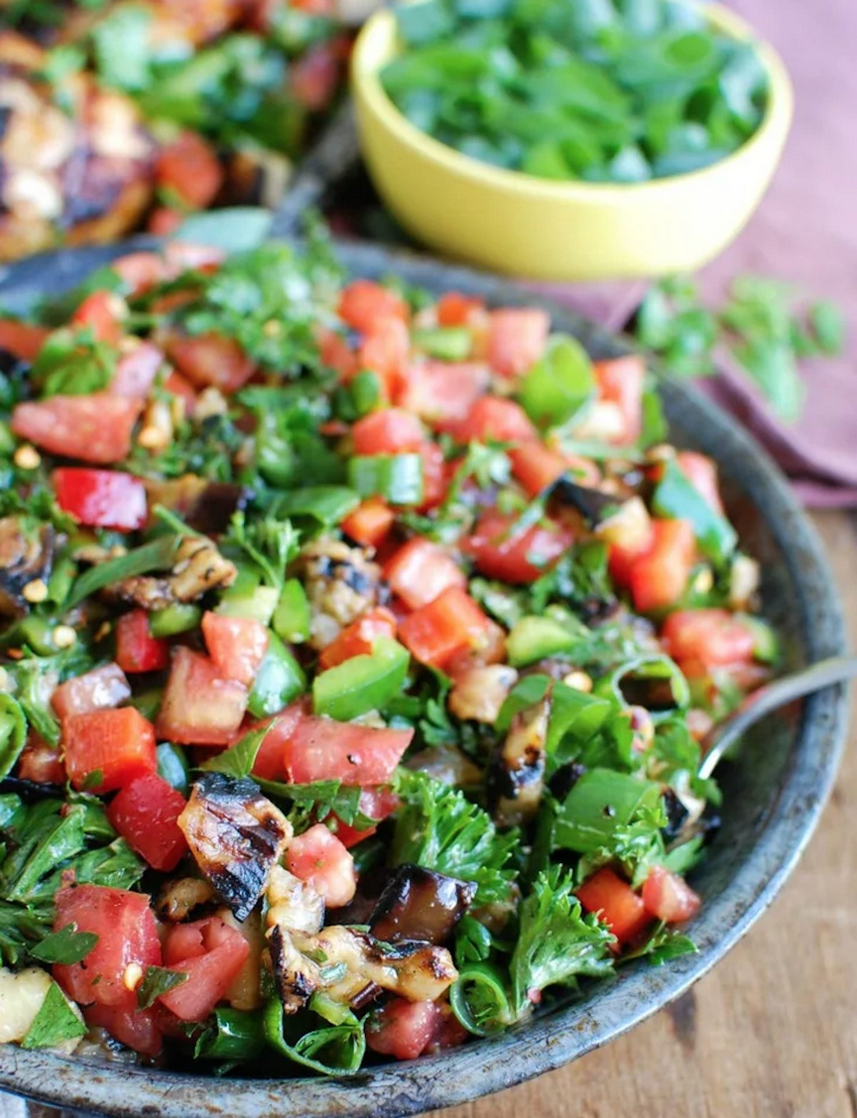 Mediterranean Salad with lots of diced tomatoes on top, in a dark blue bowl with silver spoon.