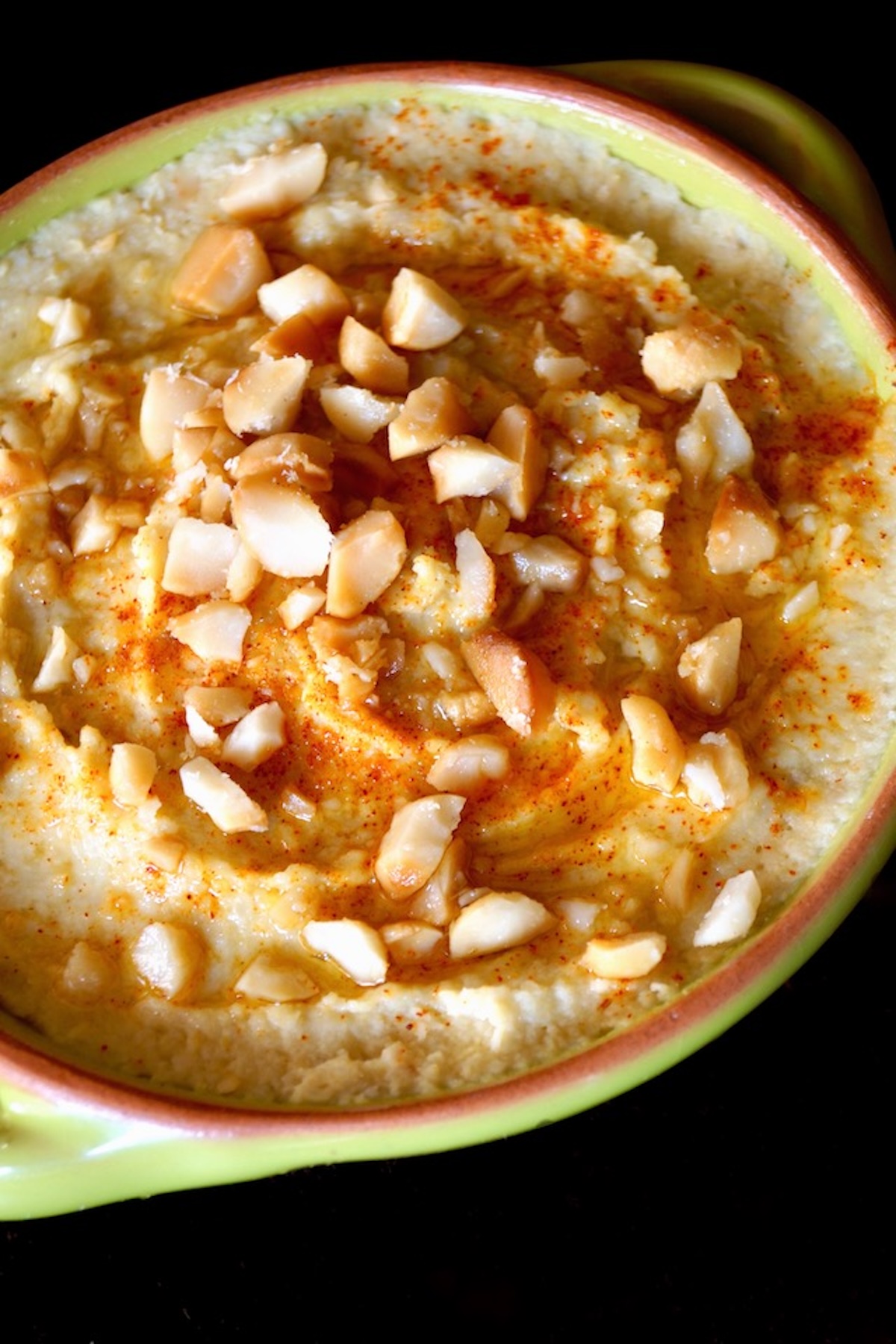 Roasted Macadamia Nut Hummus Recipe Close up of Macadamia Nut Hummus in a green bowl, with chopped nuts on top.