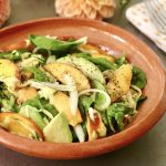Terra cotta bowl with peach avocado salad and fresh flowers behind it.