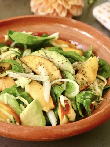 Terra cotta bowl with peach avocado salad and fresh flowers behind it.