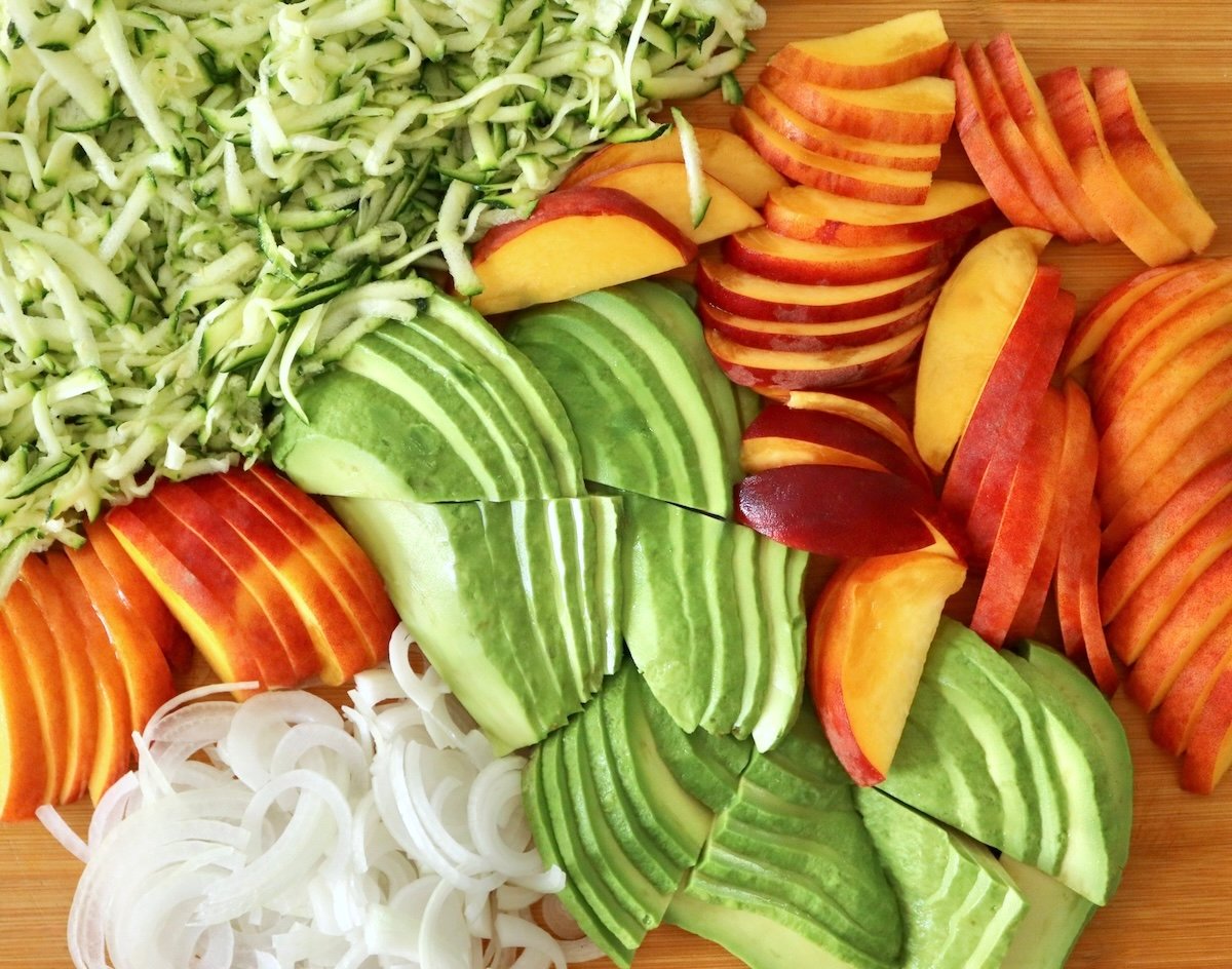Thinly sliced avocado, peach and onion, grated zucchini - on a cutting board.