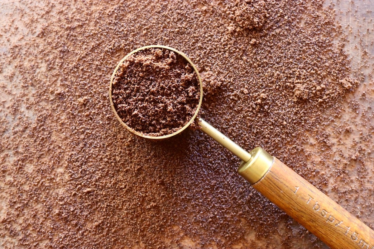 Espresso powder in a tablespoon and sprinkled around it on wooden surface.