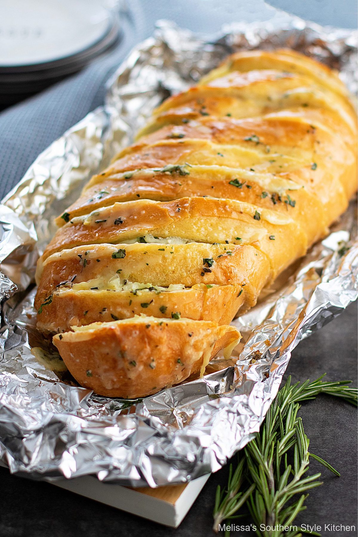 Cheesy sliced bread on foil with herbs.