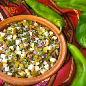 Hatch Chile Salsa with Fresh peaches in a terra cotta bowl on an orange stirped cloth with fresh raw Hatch chiles.