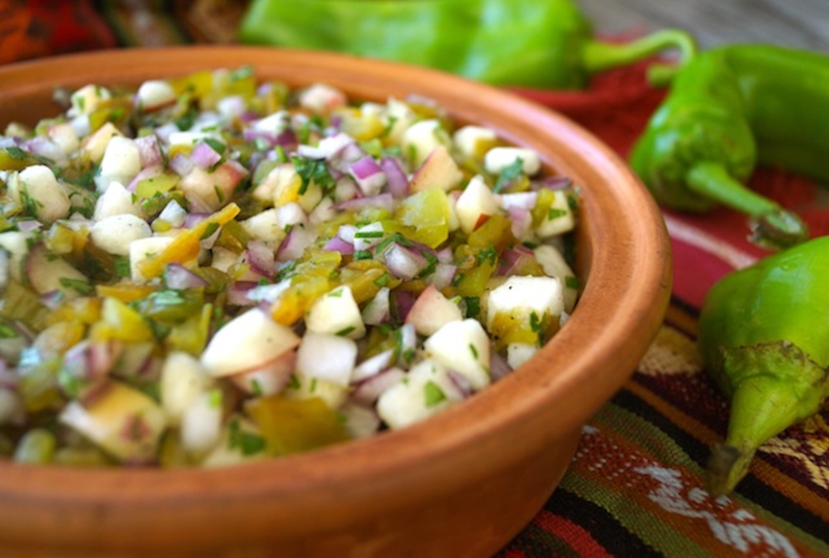 Side view of white peach and hatch chile salsa in a terra cotta bowl.