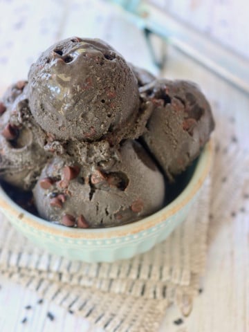 4 scoops of Black Sesame Ice Cream with chocolate chips in a mint-colored bowl with a white background.