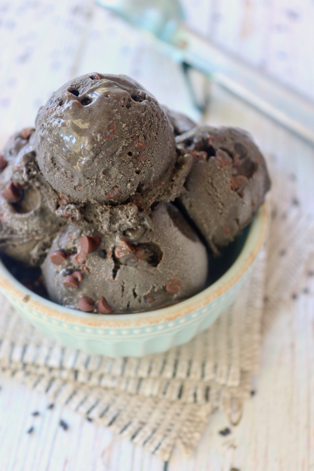 4 scoops of Black Sesame Ice Cream with chocolate chips in a min-colored bowl with a white background.