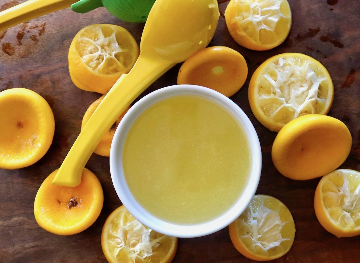 Several lemon halves and a hand juicer, with a white bowl filled with lemon juice.