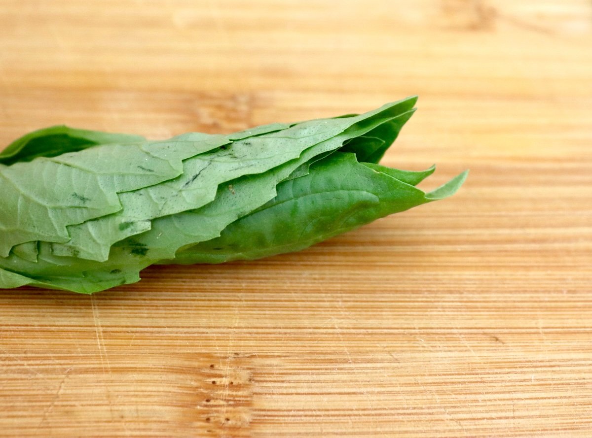 Rolled stack of fresh basil leaves on a cutting board.