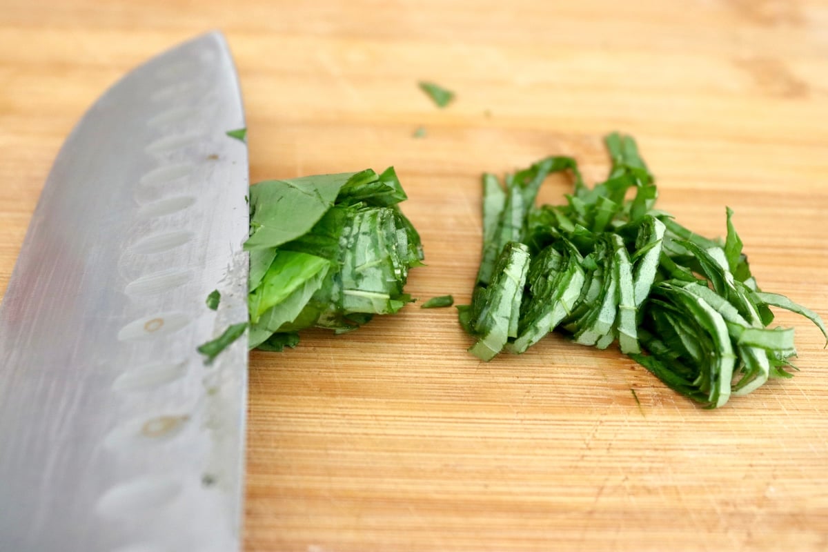 Basil chiffonade with a Chef's knife on a cutting board.