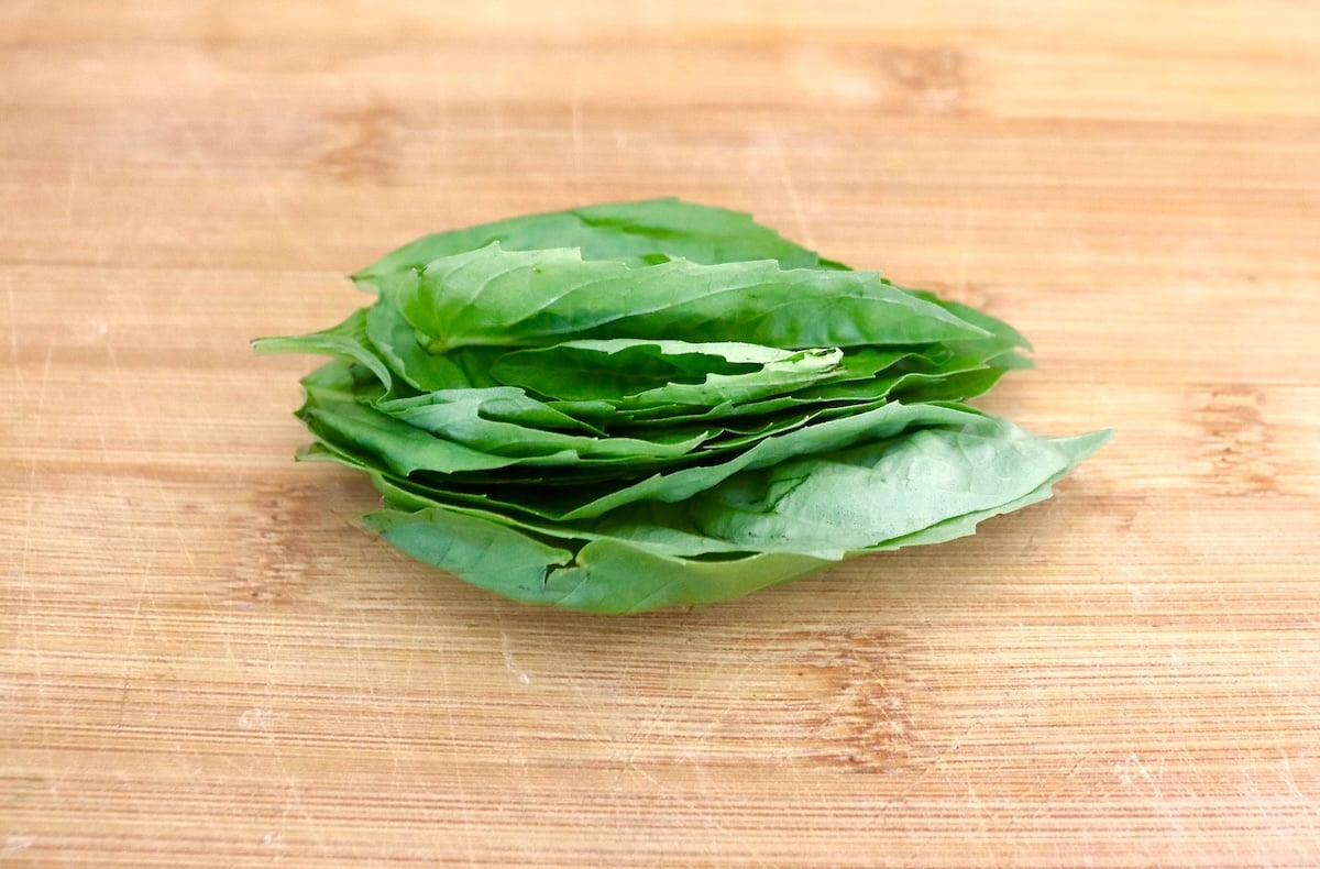 Small pile of fresh basil leaves on a cutting board.