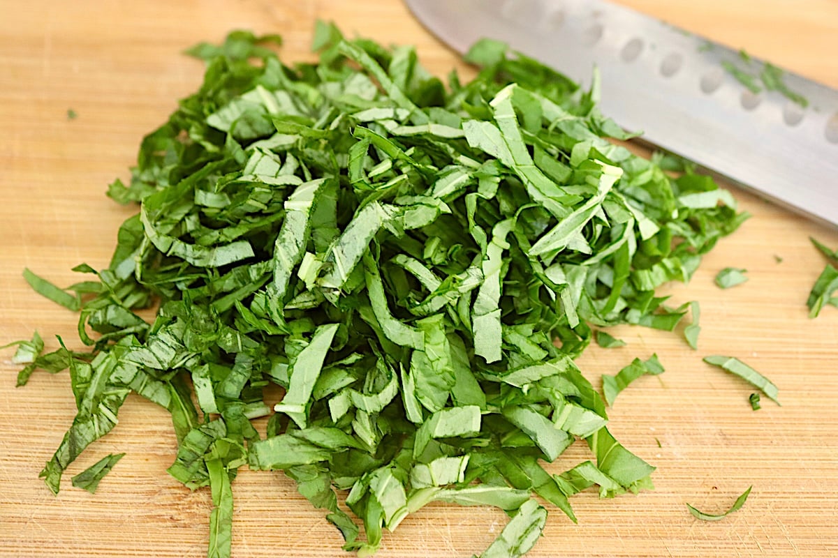Big pile of basil cut into thin strips on a cutting board.