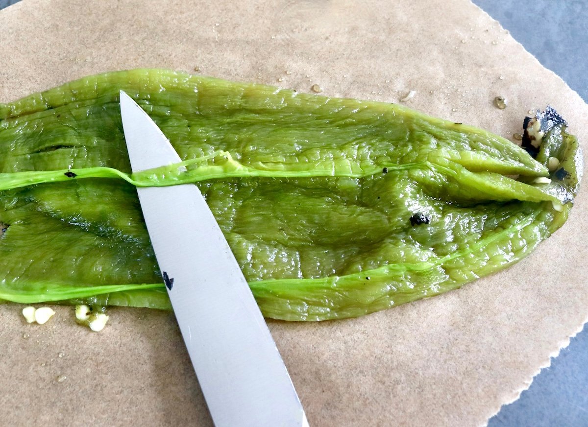 One green chili with membrane being removed by a paring knife.