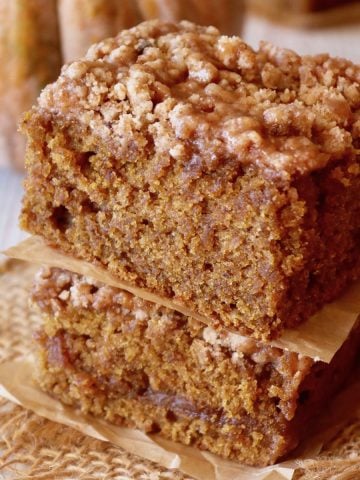 Two stacked pieces of pumpkin coffee cake with a dull orange pumpkin in the background.