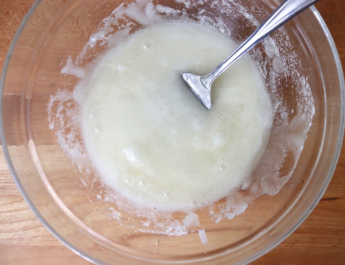 MIx of sugar and egg whites in a glass bowl with a fork.