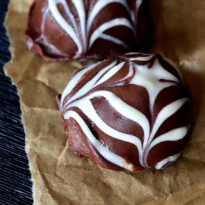 Two dark chocolate truffles with a white chocolate spiderweb on top, on parchment.