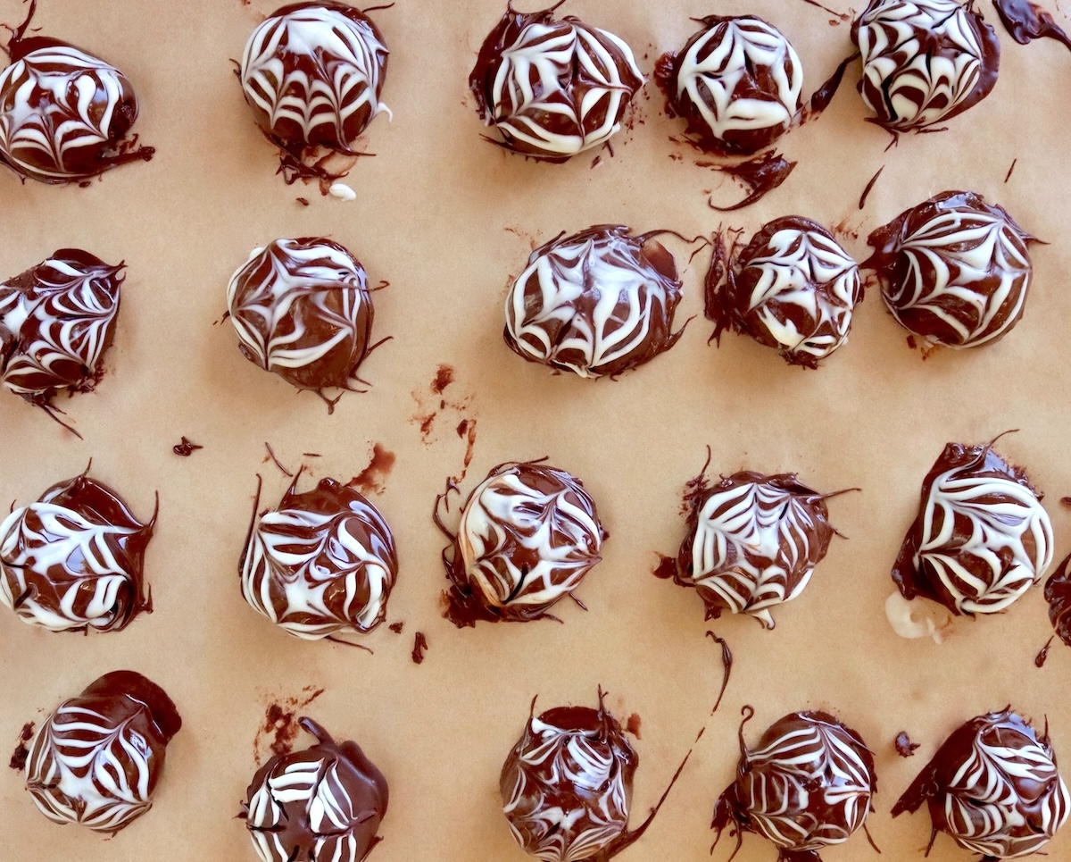 Parchment-lined sheet pan full with freshly made chocolate truffles with a halloween spider pattern on top.
