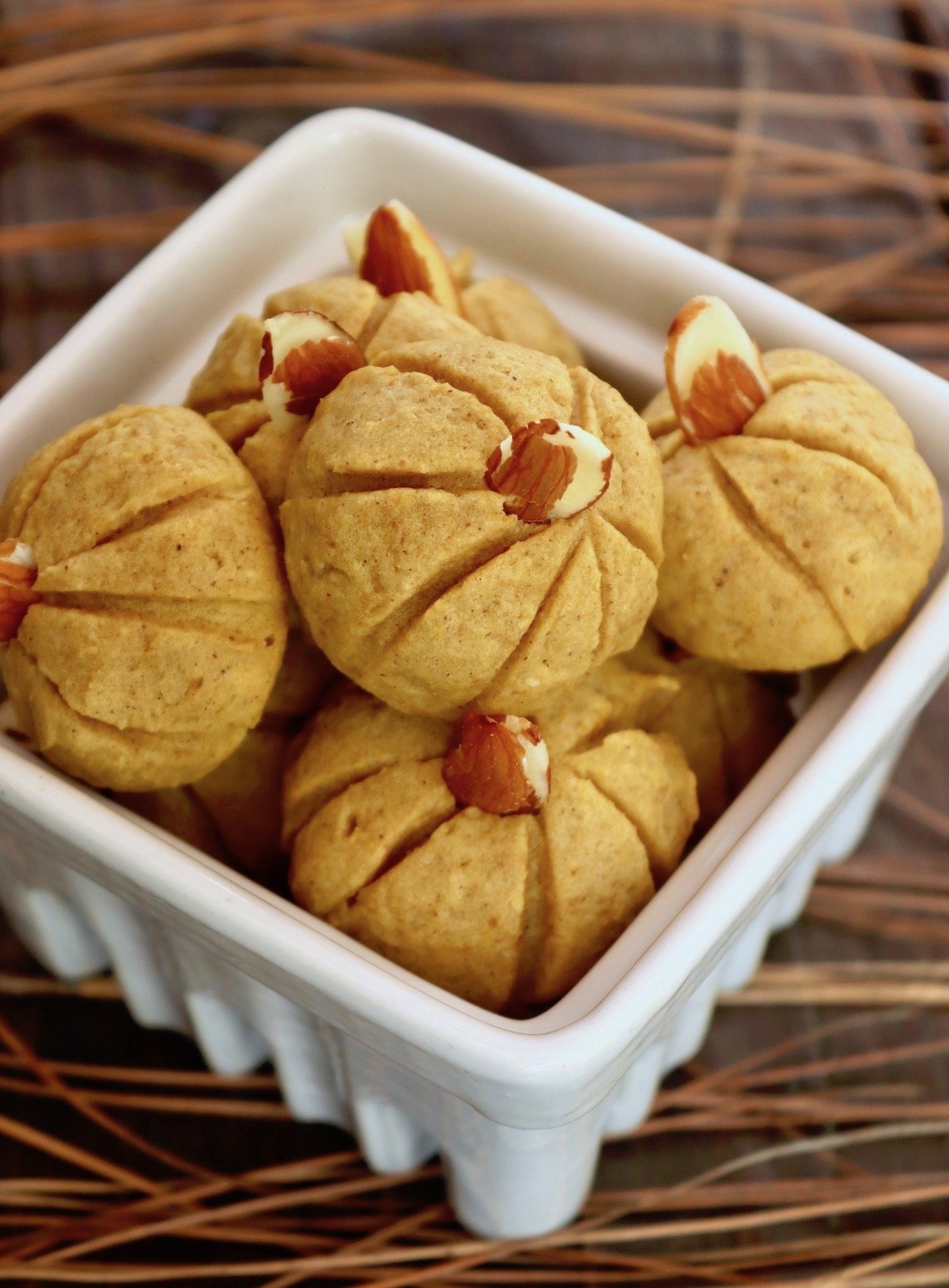 Several Pumpkin Almond Flour cookies in a white ceramic box on wood surface.