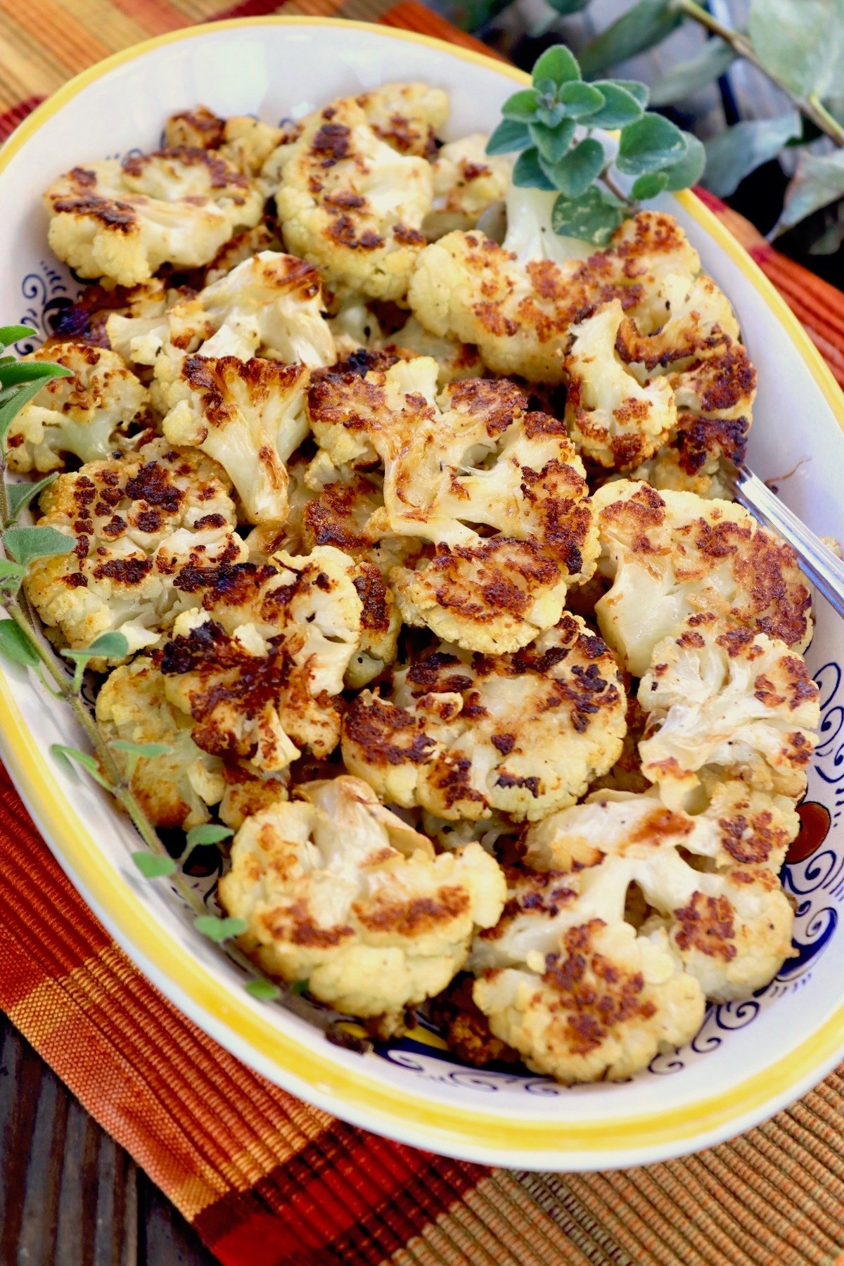 Crispy caramelized cauliflower on a ceramic yellow-rimmed, oval plate.