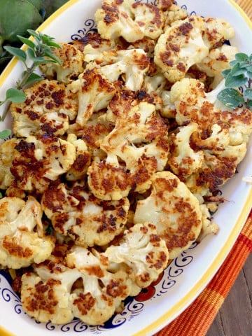 Top view of smashed golden brown cauliflower florets in a yellow-rimmed serving dish.