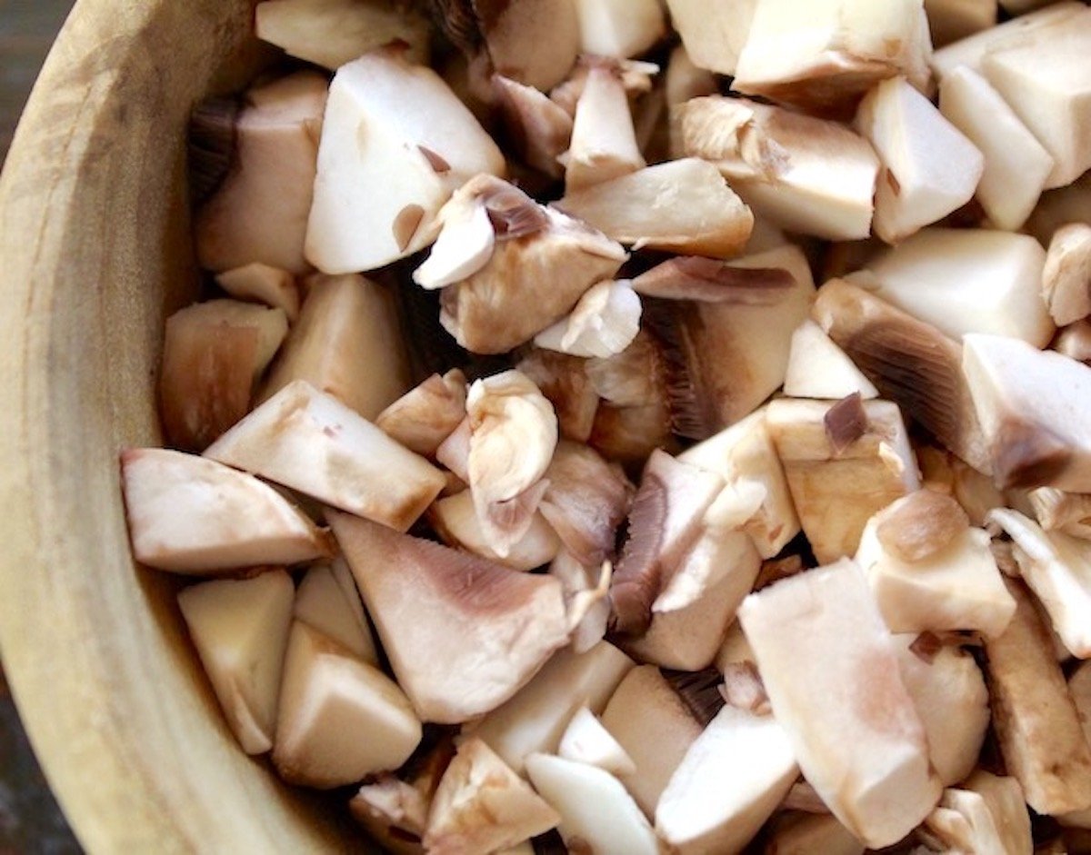 Wooden bowl filled with quartered button mushrooms.