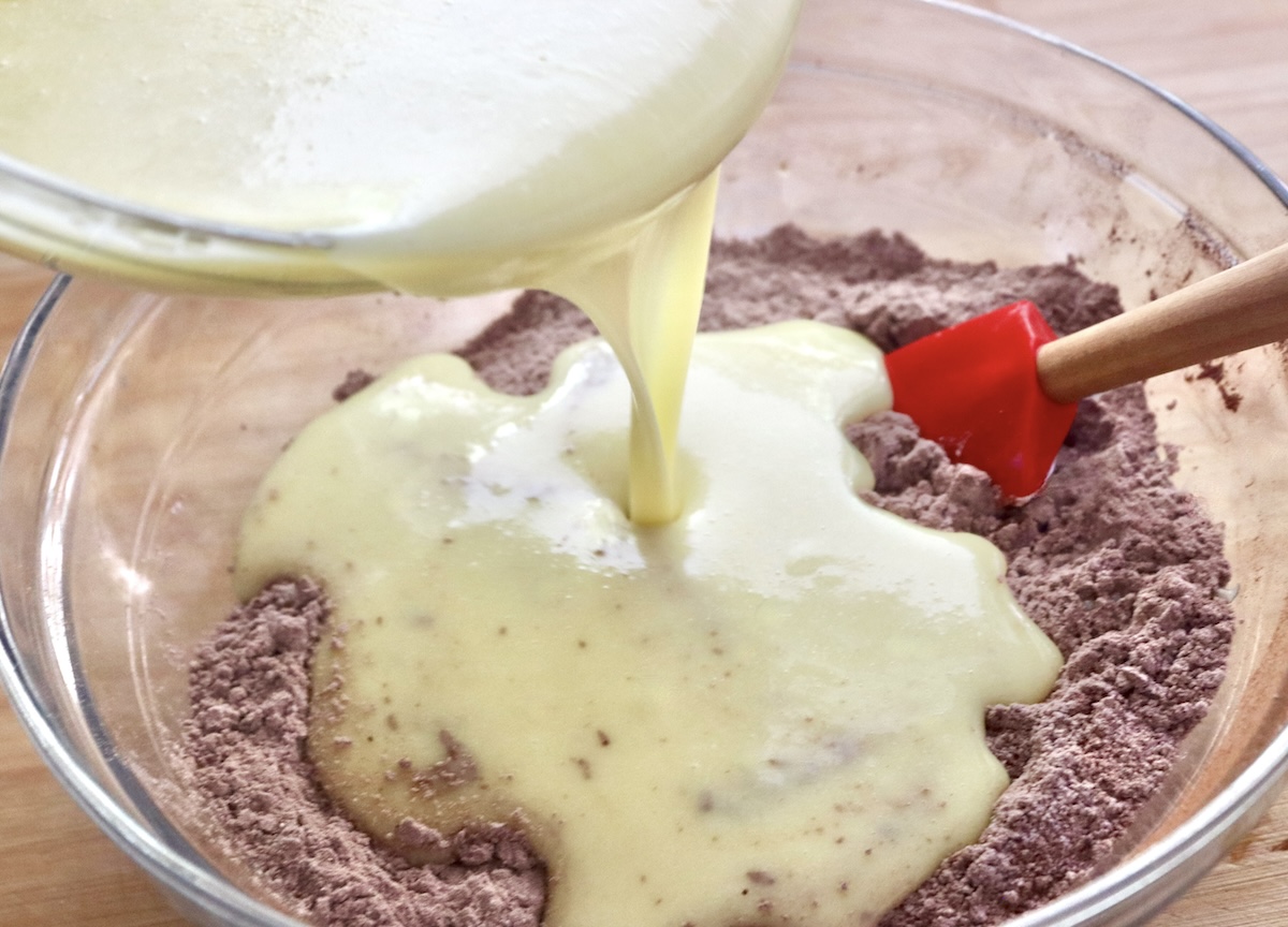 Wet egg ingredients being poured into chocolate dry ingredients for gluten-free chocolate cake.