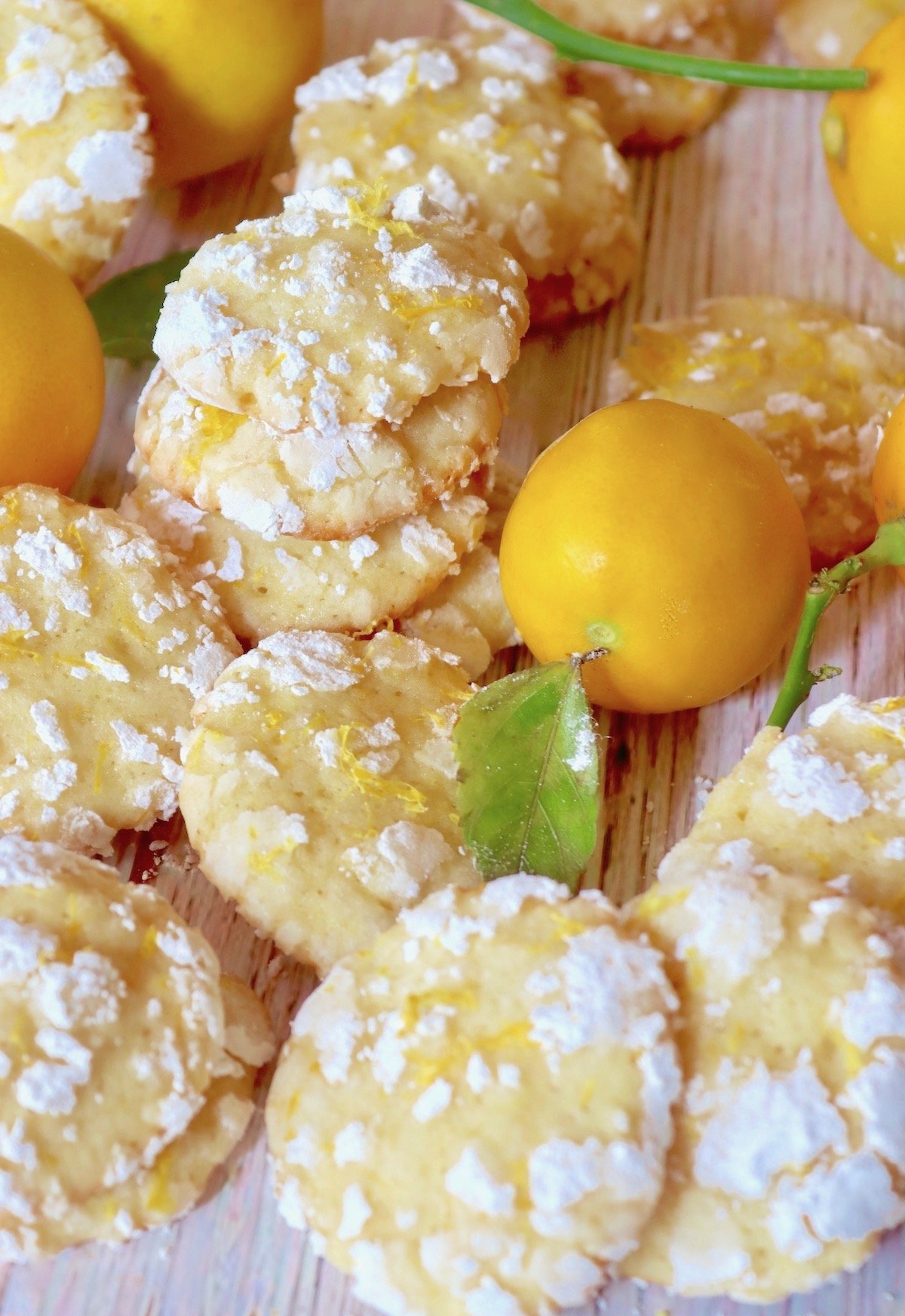 Several Meyer Lemon Crinkle Cookies surrounded by lemons.